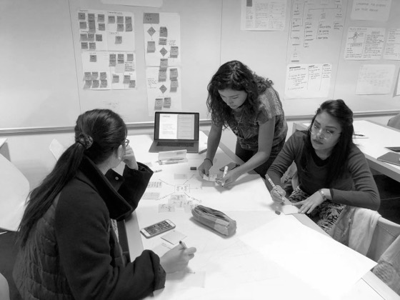 Team mapping ideas on paper at a table, with user flows and a proto-persona pinned on the wall